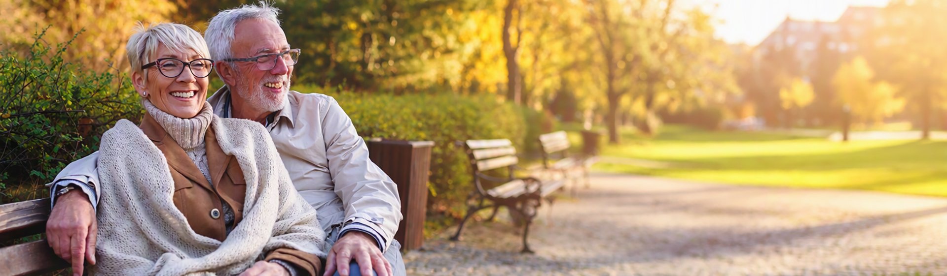 Two older adults sitting together on a park bench in autumn.