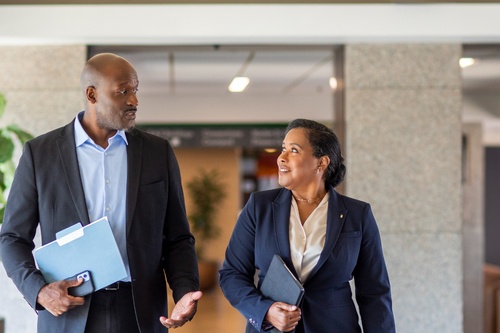 Two professionals walking side by side through a modern office corridor