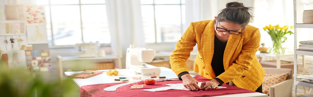 A young woman in business attire cuts out a sewing pattern on a drafting table. 
