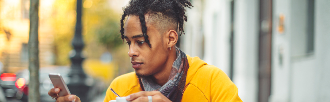 A young man holds his coffee while looking at his cellphone