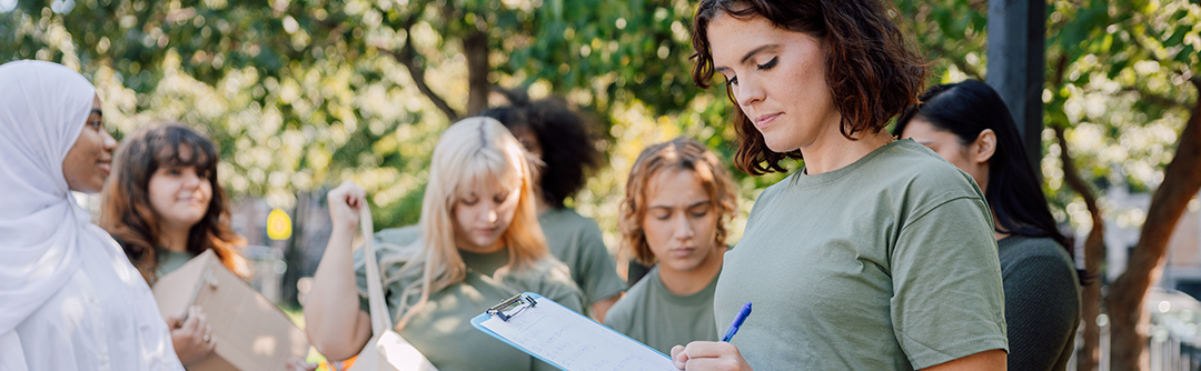A young woman is holding a clipboard, surrounded by other young adult volunteers.