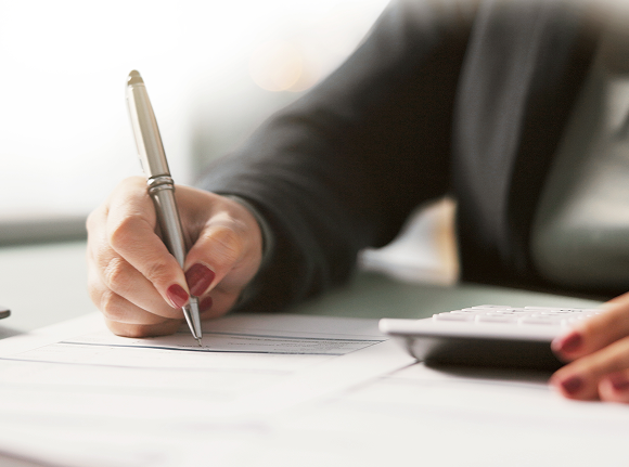 person writing on a piece of paper and using a calculator